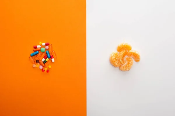 Vue du dessus des pilules colorées et mandarine sur blanc et orange — Photo de stock