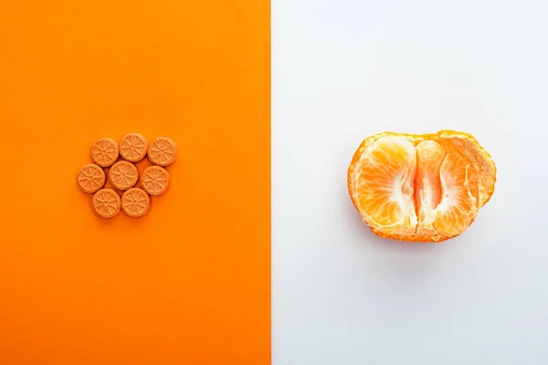 Draufsicht auf Pillen und Mandarinenhälfte auf weißem und orangefarbenem Hintergrund — Stockfoto