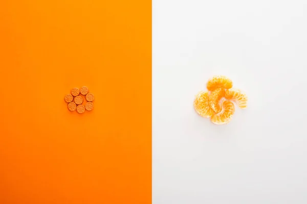 Vue du dessus des pilules brillantes et de la mandarine sur fond blanc et orange — Photo de stock