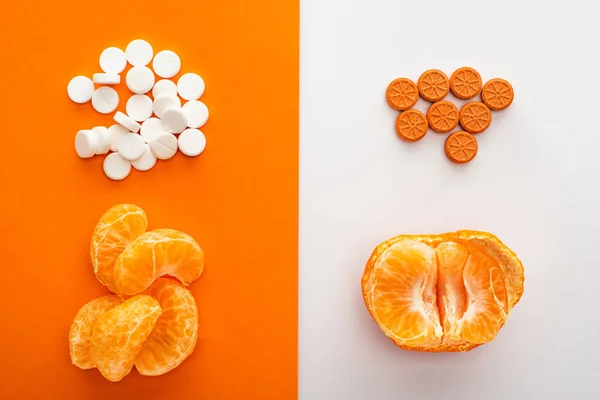 Top view of dietary supplements and mandarin on white and orange background — Stock Photo