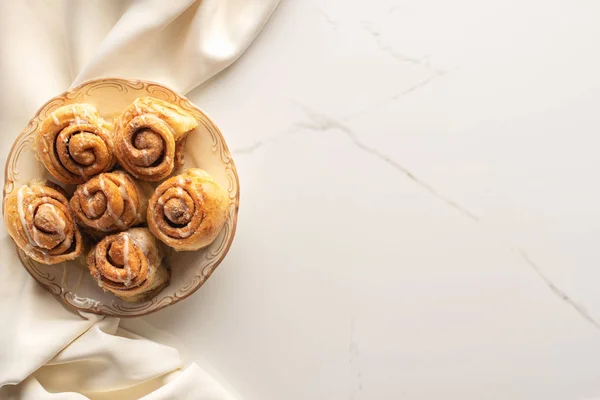 Top view of fresh homemade cinnamon rolls on marble surface with silk cloth — Stock Photo