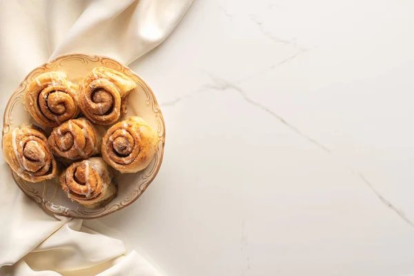 Vue de dessus des rouleaux de cannelle frais faits maison sur la surface du marbre avec du tissu de soie — Photo de stock