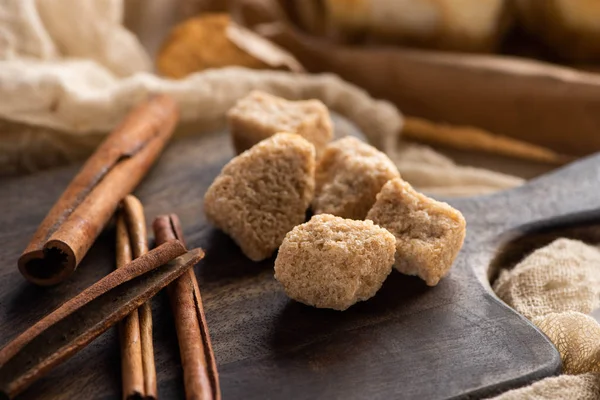 Закрыть вид на свежие коричные палочки и коричневый сахар на деревянной доске — стоковое фото