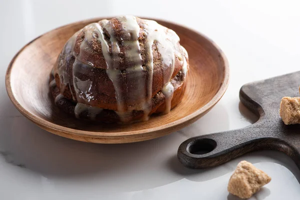 Frische hausgemachte Zimtrolle auf Teller auf Marmoroberfläche mit Schneidebrett mit braunem Zucker — Stockfoto