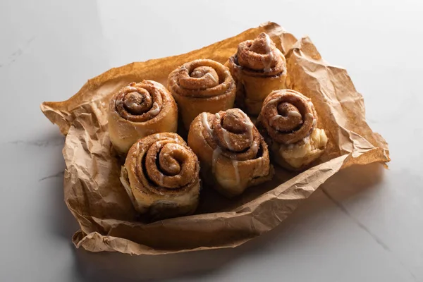 Fresh homemade cinnamon rolls on parchment paper on marble surface — Stock Photo