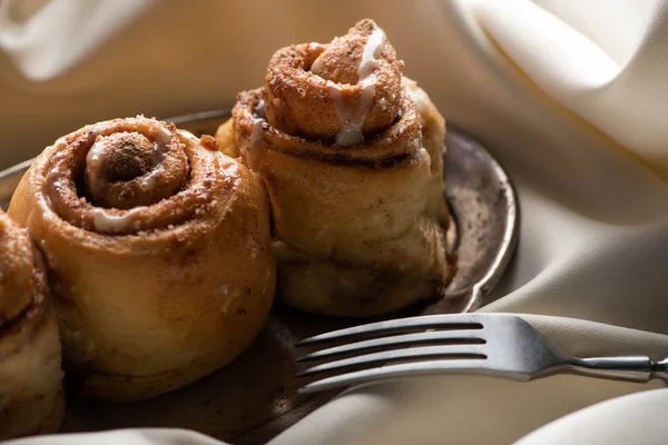 Close up view of fresh homemade cinnamon rolls on board on satin cloth with fork — Stock Photo