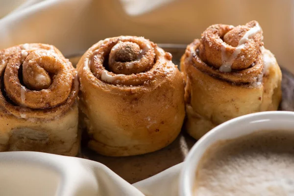 Close up view of fresh homemade cinnamon rolls on board on satin cloth with coffee — Stock Photo