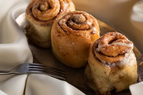 Close up view of fresh homemade cinnamon rolls on board on satin cloth with fork — Stock Photo