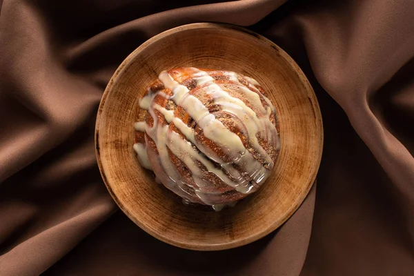 Top view of fresh homemade cinnamon roll on plate on silk brown cloth — Stock Photo