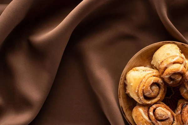 Top view of fresh homemade cinnamon rolls on plate on silk brown cloth — Stock Photo