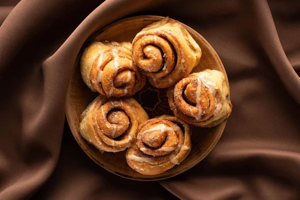 Vue du dessus des rouleaux de cannelle frais faits maison sur plaque sur tissu brun soie — Photo de stock