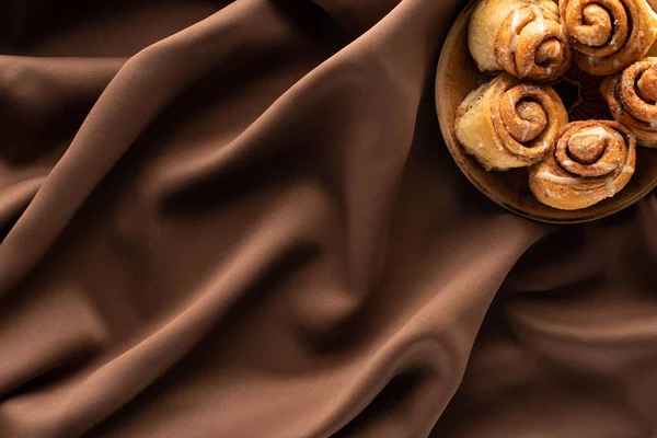 Vue de dessus des rouleaux de cannelle maison fraîche sur tissu brun soie — Photo de stock