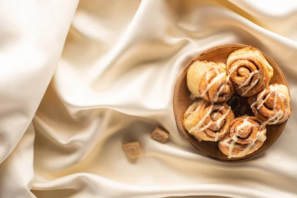 Vue de dessus des rouleaux de cannelle maison fraîche sur tissu blanc de soie avec sucre brun — Photo de stock