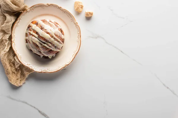 Vue de dessus du rouleau de cannelle maison fraîche sur plaque sur la surface de marbre avec sucre brun et tissu — Photo de stock