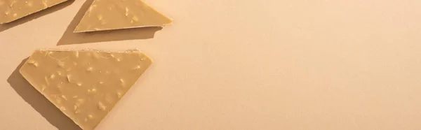 Top view of delicious broken white chocolate bar on beige background, panoramic shot — Stock Photo