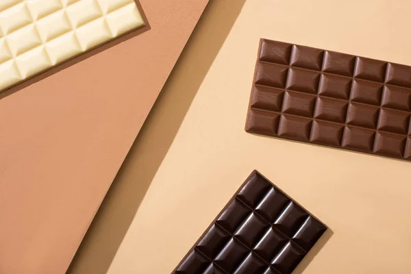 Vista dall'alto di deliziose barrette di cioccolato bianco, al latte e fondente su sfondo beige — Foto stock