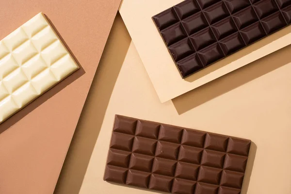 Vista dall'alto di deliziose barrette di cioccolato bianco, al latte e fondente su sfondo beige — Foto stock