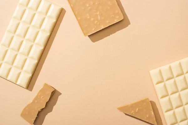 Vista dall'alto di deliziose barre di cioccolato bianco rotte e intere su sfondo beige — Foto stock