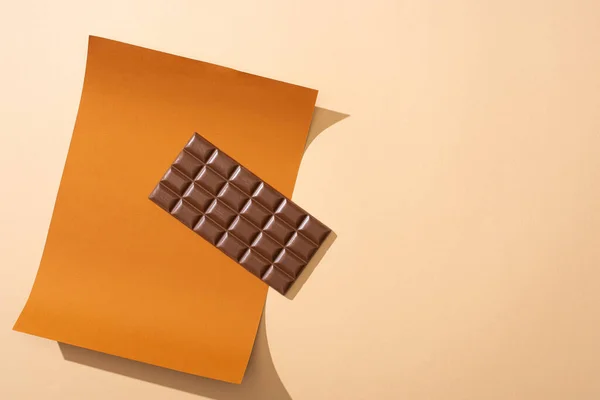 Top view of delicious milk chocolate bar on paper on beige background — Stock Photo