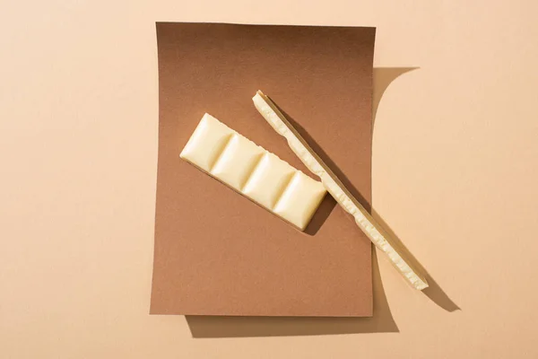 Vista superior de deliciosos pedaços de barra de chocolate branco em papel no fundo bege — Fotografia de Stock