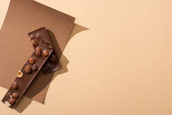 Top view of delicious  milk chocolate with nuts pieces on paper on beige background — Stock Photo