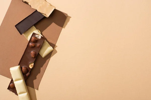 Vista dall'alto del delizioso cioccolato fondente, bianco e al latte con noci su carta su sfondo beige — Foto stock