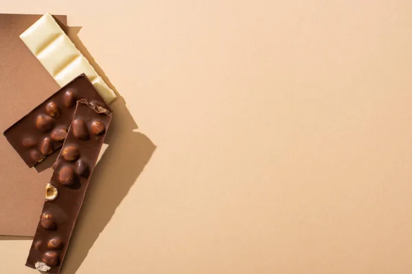 Вид сверху на вкусный белый и молочный шоколад с орехами на бумаге на бежевом фоне — стоковое фото