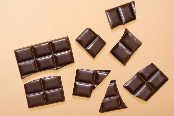 Vista dall'alto di deliziosa barra di cioccolato fondente rotto su sfondo beige — Foto stock