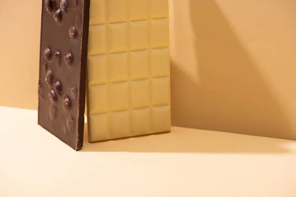 Köstliche weiße und dunkle Schokoladentafeln mit Nüssen auf beigem Hintergrund — Stockfoto