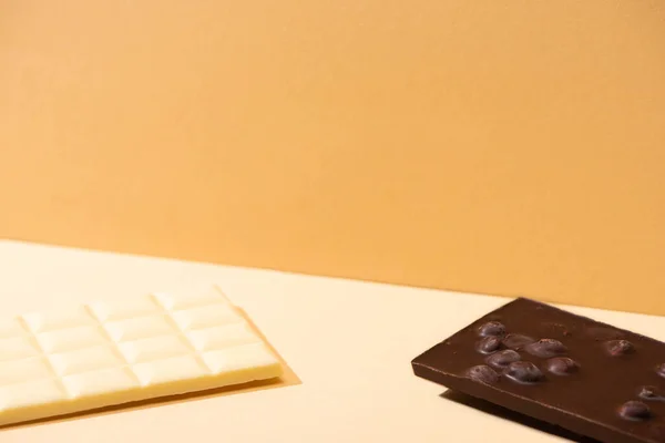 Deliziose barrette di cioccolato bianco e fondente rotte con noci su sfondo beige — Foto stock