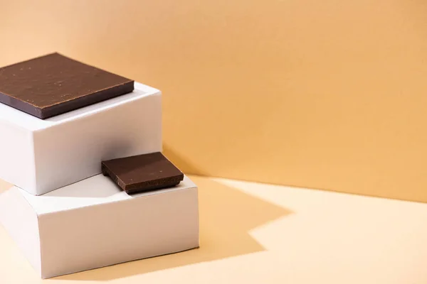 Вкусные кусочки темного шоколада и квадратные кубики на бежевом фоне — стоковое фото