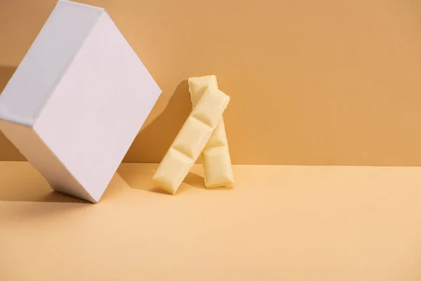 Вкусные кусочки белого шоколада и кубик на бежевом фоне — стоковое фото