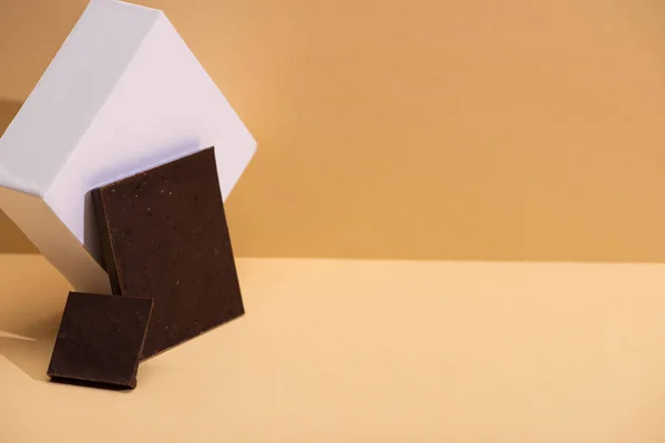 Delicious dark chocolate pieces and cube on beige background — Stock Photo