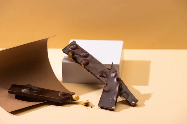 Delizioso cioccolato fondente con pezzi di noci, carta e cubo su sfondo beige — Foto stock