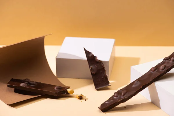 Смачний темний шоколад з шматочками горіхів, папером та кубиками на бежевому фоні — стокове фото