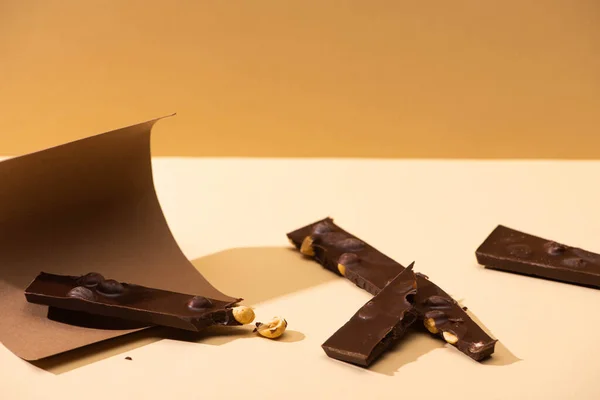Delicioso chocolate negro con piezas de frutos secos, papel sobre fondo beige - foto de stock