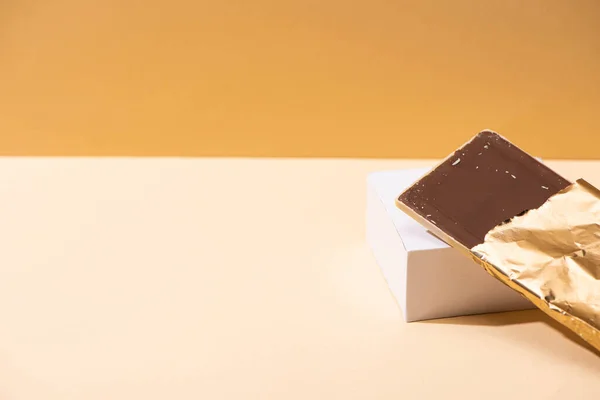 Deliziosa barretta di cioccolato al latte in lamina dorata su cubo su sfondo beige — Foto stock