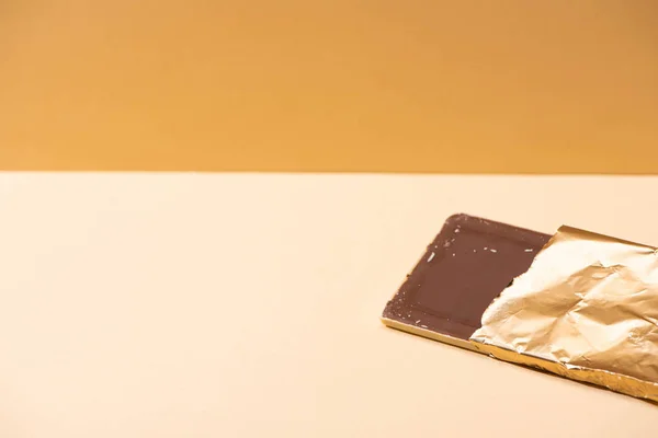 Delicious milk chocolate bar in golden foil on beige background — Stock Photo