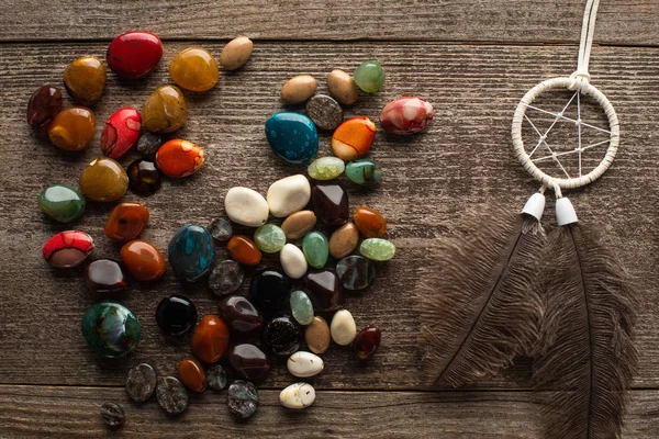 Top view of fortune telling stones and dreamcatcher with feathers on wooden surface — Stock Photo