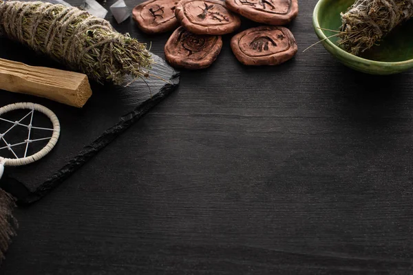 Clay amulets near shamanic smudge sticks and dreamcatcher on dark wooden surface — Stock Photo