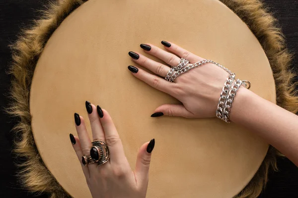 Top view of shaman with jewelry rings and chain on hands playing on tambourine isolated on black — Stock Photo