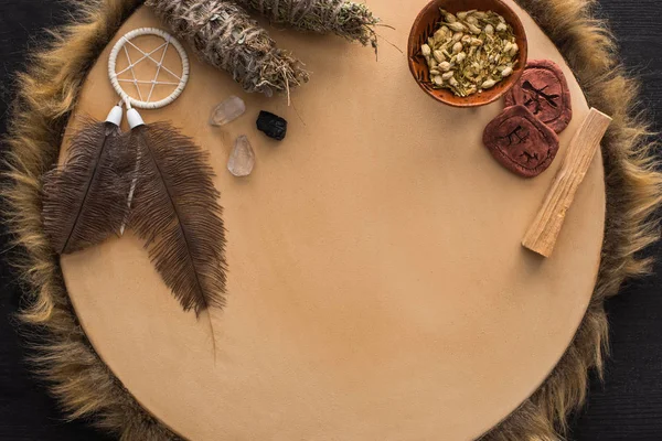 Vista dall'alto di bastoncini di sbavatura con fiori secchi, acchiappasogni e amuleti di argilla su tamburello su superficie di legno scuro — Foto stock