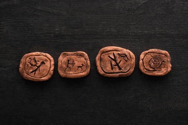 Vue de dessus des amulettes d'argile avec des symboles sur fond en bois noir — Photo de stock