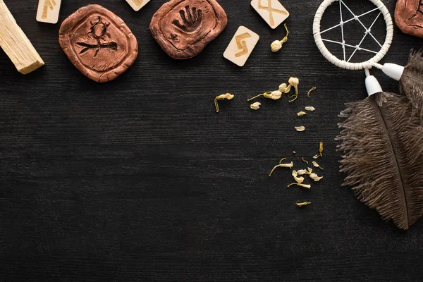 Top view of runes, dreamcatcher and dry flowers on dark wooden surface — Stock Photo