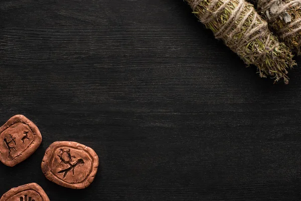 Top view of clay amulets with herbal smudge sticks on dark wooden background — Stock Photo