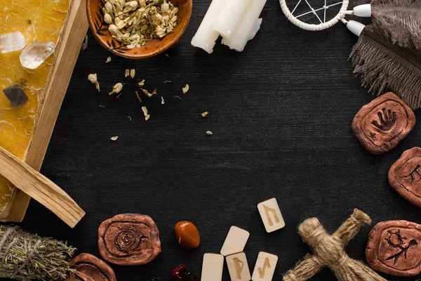 Vista superior del marco de amuletos chamánicos, libro y velas sobre fondo de madera negro — Stock Photo