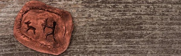 Top view of clay amulet with symbols on wooden surface, panoramic shot — Stock Photo