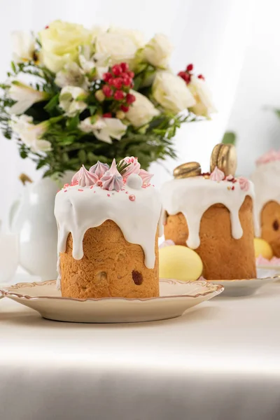 Selective focus of delicious easter cakes with golden french macaroons and meringue on icing near floral bouquet — Stock Photo