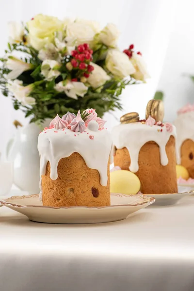 Selektiver Fokus von köstlichen Osterkuchen mit goldenen französischen Makronen und Baiser auf Zuckerguss in der Nähe von Blumenstrauß — Stockfoto