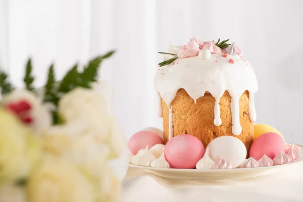 Foco seletivo de delicioso bolo de Páscoa decorado com merengue com ovos rosa e branco na placa perto de flores — Fotografia de Stock